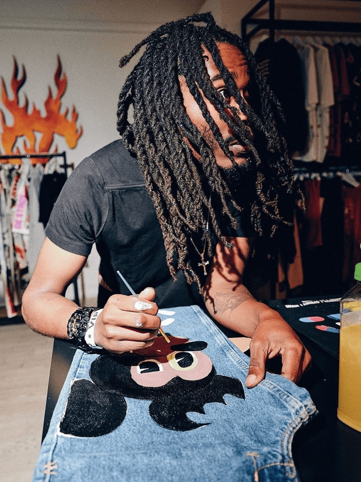 A photograph of an artist hand-painting a Mickey Mouse character onto a pair of blue denim jeans